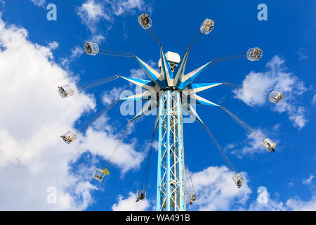 Southbank Starflyer fairground ride, tall funfair attraction, capsules swinging around central pillar against blue summer sky Stock Photo