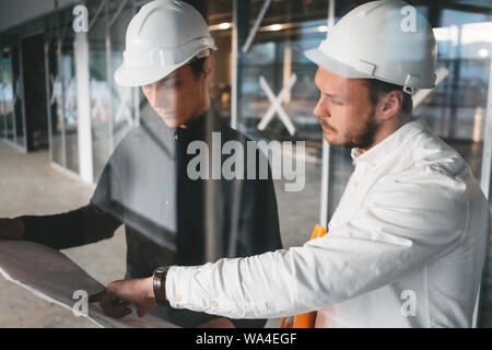 Two building engineers with blueprint working on construction site. Industrial enginer and worker looking build drawing Stock Photo