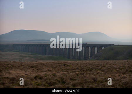Arriva Northern rail class 158 sprinter train crossing Ribblehead viaduct at sunset with Ingleborough behind