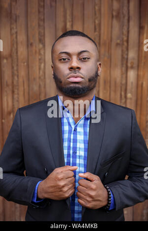 Portrait of young black bearded guy. Afro american man in suit is confident and looking at camera on dark wood background. Stock Photo