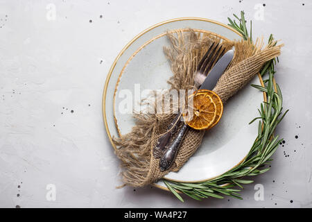 Minimalistic simple rustic table setting with empty plates, fork and knife with burlap napkin and rosemary. Top view, flat lay Stock Photo