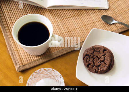 Coffee break - black coffee in white ceramic cup on wooden table with cookie, sugar, placemat, spoon and magazine, chaotic arrangement, top view Stock Photo