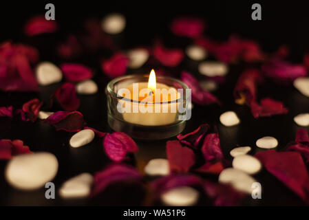 candle, red rose petals, marble stones on black background Stock Photo