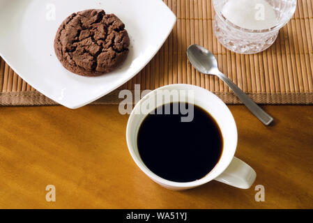 Drinking coffee in the morning - black coffee in white cup, cookie on white plate, teaspoon, bamboo placemat and sugar-bowl on wooden table, indoors Stock Photo