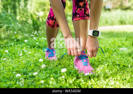 Healthy summer lifestyle - Girl runner getting ready for weight loss exercise tying running shoes laces wearing smartwatch activity tracker for an active living. Cute pink floral tights and outfit. Stock Photo