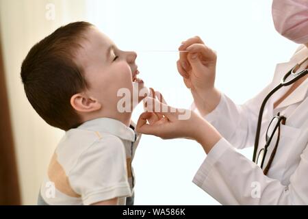 The doctor touched the tip of the nose of a laughing child as she examined her throat. The boy looked up and smiled contentedly with his eyes closed. Stock Photo