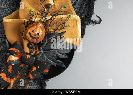 Halloween party place setting of black plate, orange napkin and novelty pumpkin decor with ribbon of orange bats on black sitting on a grey and nettin Stock Photo