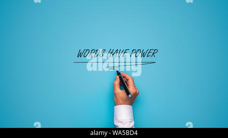 Male hand writing a Words have power sign with black marker on blue background. Stock Photo