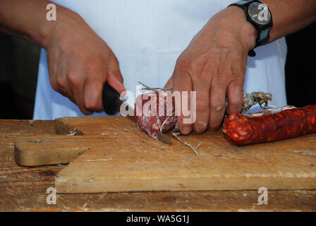 butcher cutting salami on wooden board Stock Photo