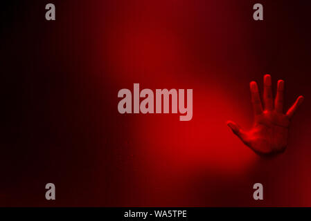 Red color filter version of Creepy man holding the frosted glass with one hand. Stock Photo