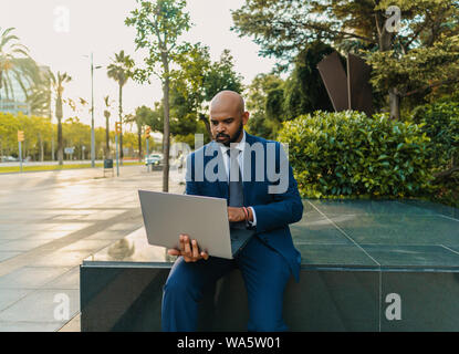 Indian businessman holding laptop notebook wearing blue suit near office Stock Photo