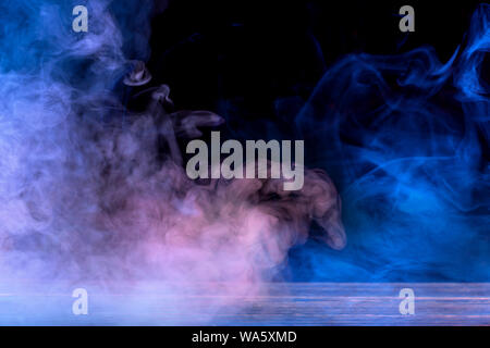 Conceptual image of multi-colored smoke isolated on dark black background and wooden table. Stock Photo