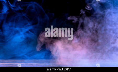 Conceptual image of multi-colored smoke isolated on dark black background and wooden table. Stock Photo