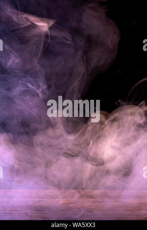 Conceptual image of multi-colored smoke isolated on dark black background and wooden table. Stock Photo
