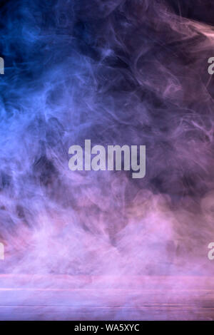 Conceptual image of multi-colored smoke isolated on dark black background and wooden table. Stock Photo