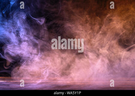 Conceptual image of multi-colored smoke isolated on dark black background and wooden table. Stock Photo