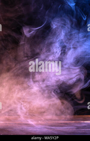 Conceptual image of multi-colored smoke isolated on dark black background and wooden table. Stock Photo
