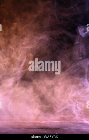 Conceptual image of multi-colored smoke isolated on dark black background and wooden table. Stock Photo
