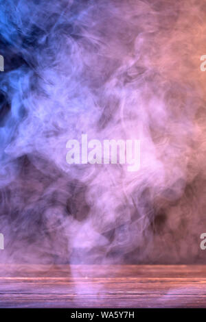 Conceptual image of multi-colored smoke isolated on dark black background and wooden table. Stock Photo
