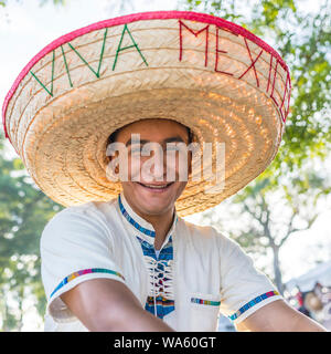 A 20 something HIspanic male wears and oversized straw sombrero hat with 'Viva Mexico' stitched on it in yarn and smiles while facing forward. Stock Photo