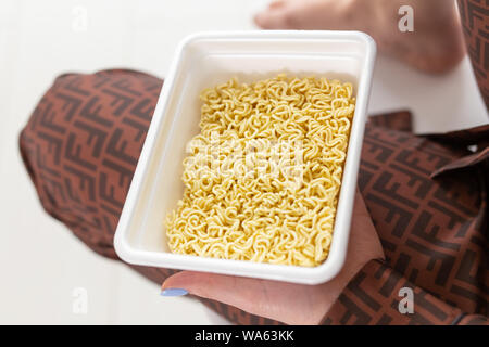 Hand holding plate with instant chinese noodles, Sodium diet high risk kidney failure. Unhealthy eating concept Stock Photo