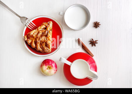 Piece of fresh apple pie on the plate with fork, fresh apple, spices, milk jug close up Stock Photo