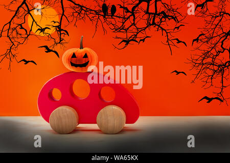 Toy red wooden car carries a spooky pumpkin. Happy Halloween concept Stock Photo