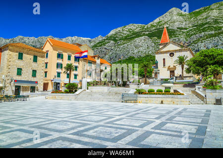 Popular mediterranean resort with beautiful old city center. Street cafees and catholic christian church in town square. High Biokovo mountains in bac Stock Photo