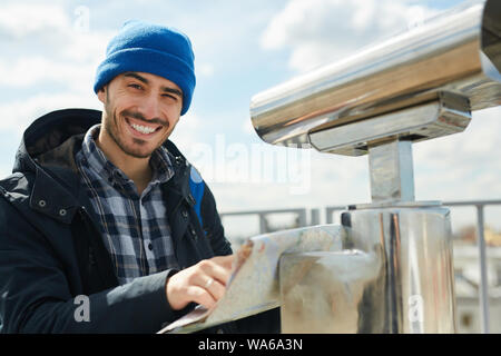 Portrait of handsome male tourist holding map and looking at camera while standing on rooftop viewing platform Stock Photo