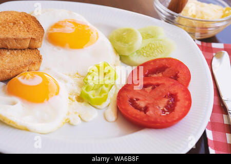 Breakfast - fried eggs, butter and tomato in white plate. Close up image Stock Photo