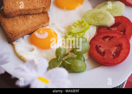 Breakfast - fried eggs, butter and tomato in white plate. Close up image Stock Photo