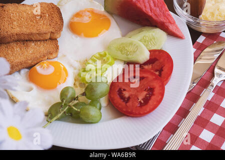 Breakfast - fried eggs, butter and tomato in white plate. Close up image Stock Photo