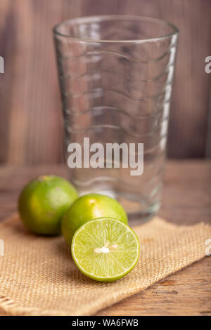 Close up a half of the green lime place on the woven sack and blerred empty glass in a kitchen. Select focus shallow depth of field. Lemon is a kind o Stock Photo