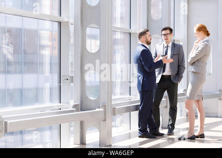 Businessmen and businesswoman talk about business holding coffee in hand at break in office Stock Photo