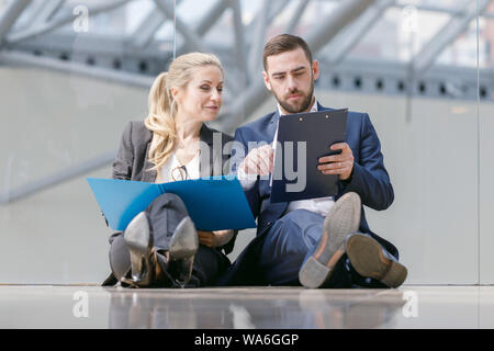 Two business people at break in office sitting on the floor and discuss working documents Stock Photo