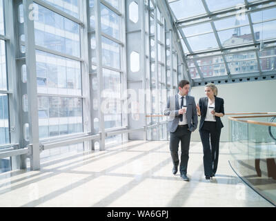 Businessman and businesswoman walk together and talk about business holding coffee in hand Stock Photo
