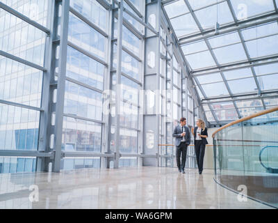 Businessman and businesswoman walk together and talk about business holding coffee in hand Stock Photo