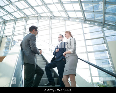 Business people team standing together on escalator and talk about business holding coffee in hand Stock Photo