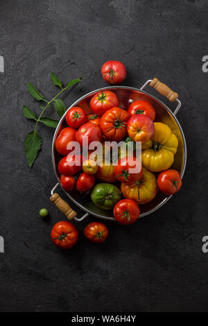 Ripe tomatoes in a pan on black stone background, copy space. Stock Photo