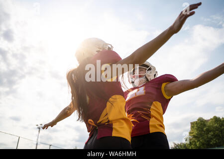 Photo of two American football athletes wearing helmets with their hands to side against cloudy sky Stock Photo
