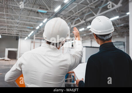 Builder worker and safety inspector wearing helment have meeting while look on construction blueprint. Two engineers building under constuction Stock Photo
