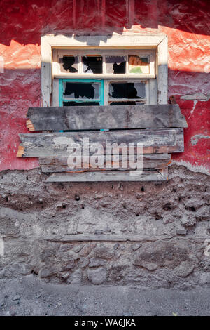 Window with broken glass and barred shut with planks on red wall of an abandoned shanty house Stock Photo