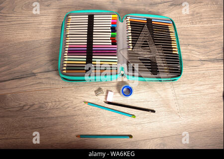 Open pen case with many pencils. Triangle rulers, roll of tape, pencil sharpener and pencils spread out on wooden table. Horizontal image with copy sp Stock Photo