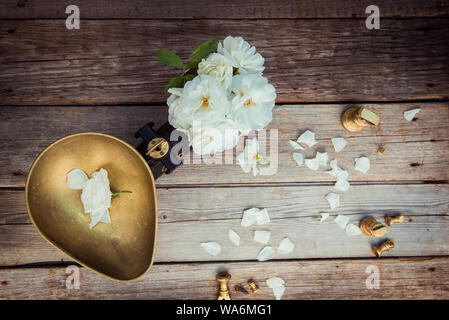 Top view antique vintage measuring scale weights with fresh white tea rose flowers on the rustic wooden background. Nature ingredients. Pure and simpi