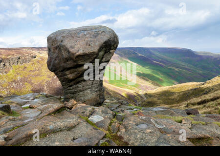 An eroded gritstone boulder and a view along Grindsbrook Clough and part of the southern edge of Kinder Scout, Derbyshire, Peak District, England, UK Stock Photo