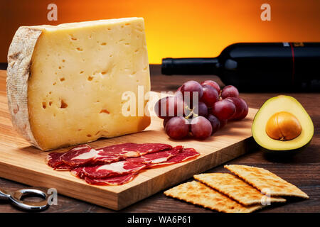 Aged cheese on wooden table with wooden cutting board., ham, fruits and crackers Stock Photo
