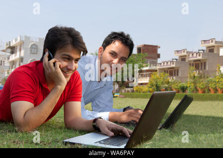 Young men lying on grass in lawn and using laptops Stock Photo