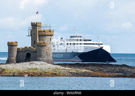 After a run from Liverpool, high-speed ferry Manannan passes the Refuge Tower on St Mary's Isle at the entrance to Douglas Harbour on the Isle of Man. Stock Photo