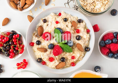 oatmeal porridge with fresh berries, nuts, honey and mint in a bowl for healthy diet breakfast. top view Stock Photo