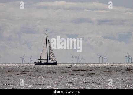 Felixstowe, Suffolk, UK - 18 August 2019: Sailing dinghy heading for Harwich harbour. Gunfleet Sands offshore wind farm off Clacton is visible in the distance. Stock Photo
